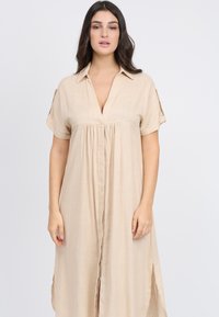 Abito camicia in lino beige con maniche corte, scollatura a V e chiusura frontale a bottoni. Presenta delle fessure laterali per facilitare il movimento; tessuto leggero.