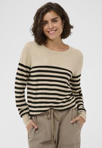 Beige og sortstribet sweater med rund halsudskæring og lange ærmer, kombineret med beige bukser med snørre. Blødt stof, afslappet design.