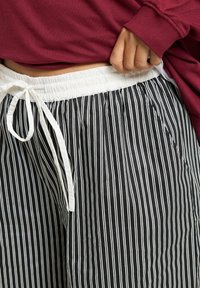 Svart- och vitrandiga byxor med elastisk midja och snörning. Har sidofickor och en lätt, glatt textur.