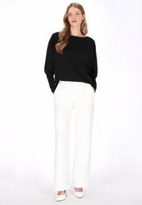 Haut à manches longues noir en tissu doux, associé à un pantalon large blanc. La tenue présente une coupe décontractée et un design épuré.