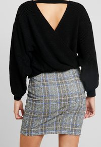 Schwarzer gestrickter Pullover mit V-Ausschnitt, kombiniert mit einem figurbetonten karierten Minirock mit blauen und grünen Akzenten.