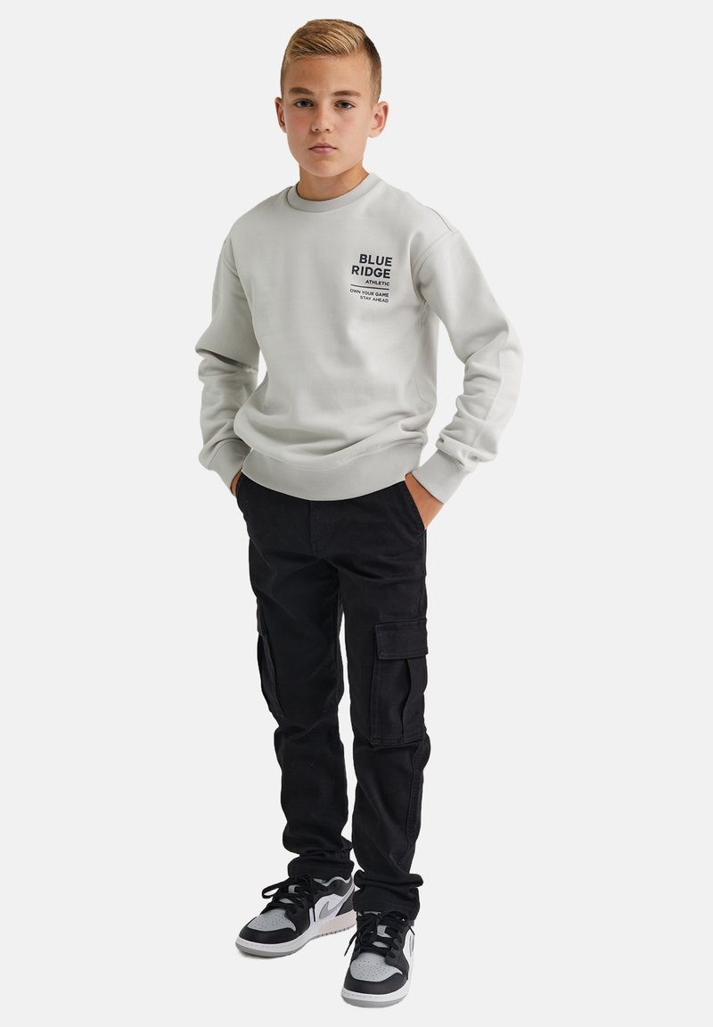 Svetlošedý sveter s nápisom "BLUE RIDGE", spojený s čiernymi cargo nohavicami a sivými teniskami s čiernymi akcentmi. Neformálny strih a dizajn.
