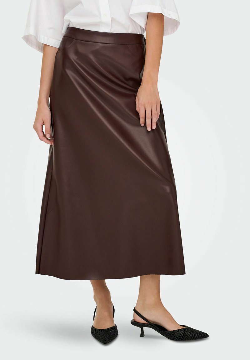 Jupe maxi en simili cuir marron avec une texture lisse, taille haute et design fluide, associée à des chaussures à talons ouverts noires à bout pointu.