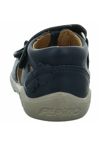 Zapato de cuero navy con diseños recortados y acentos florales. Correa de velcro y suela de goma beige, tacón redondeado para mayor comodidad.