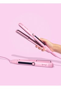 Roze haarstylers met een slank ontwerp, glanzende afwerking, afgeronde hoeken en een aan-uitknop. Snoer bevestigd, leunend tegen een zachte roze achtergrond.
