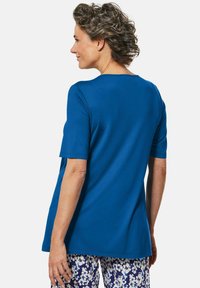 Blaues kurzärmliges Hemd aus glattem Stoff mit rundem Halsausschnitt und lockerer Passform, kombiniert mit gemusterten Blumenhosen.