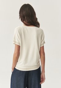 Top corta a maniche corte in crema chiaro con scollatura rotonda e dettagli a righe alle maniche e all'orlo inferiore, realizzato in tessuto morbido.