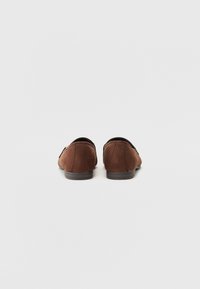 Brune semskede loafers med lav profil og rund tå. Har syddetaljer og en flad gummisål uden synligt hardware eller accenter.