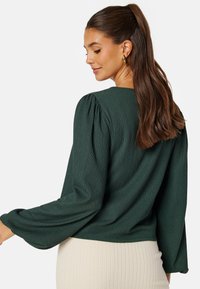 Zielona bluzka o fakturze z bufiastymi rękawami i okrągłym dekoltem, zestawiona z prążkowaną kremową spódnicą. Tkanina ma subtelny wzór.