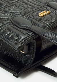 Sort quiltet lædertaske med tekstureret overflade. Har et guld logoaccent, en klaplukning og en slank skulderrem.