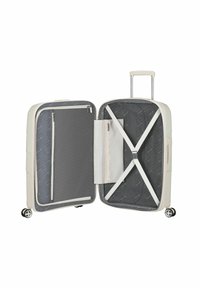 Valigia rigida color crema, con un interno grigio con cerniera, cinghie incrociate per un imballaggio sicuro e due ruote per una facile mobilità.