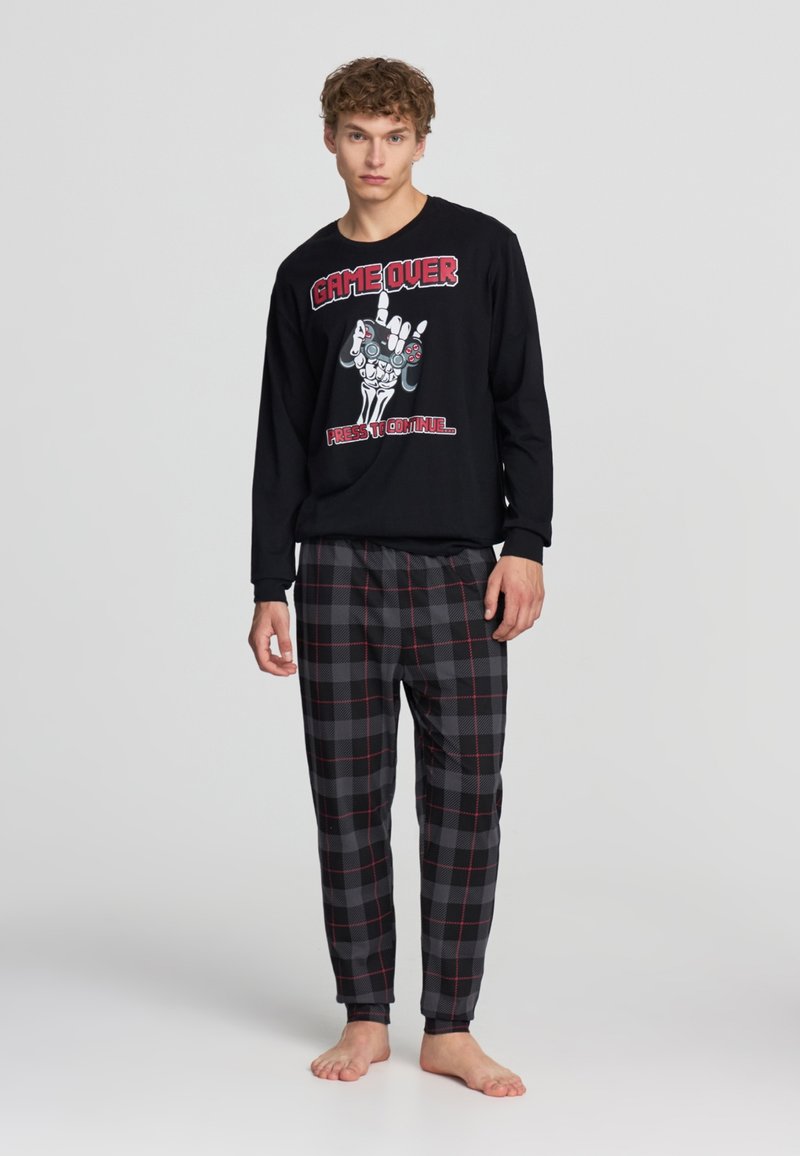 Maglietta nera a maniche lunghe con stampa grafica di una mano e controller di gioco; abbinata a pantaloni morbidi e rilassati in plaid grigio e nero.