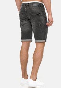 Shorts de denim gris con dobladillos enrollados, que presentan dos bolsillos traseros y una etiqueta de cuero en la cintura. Estilo casual con un ajuste slim.