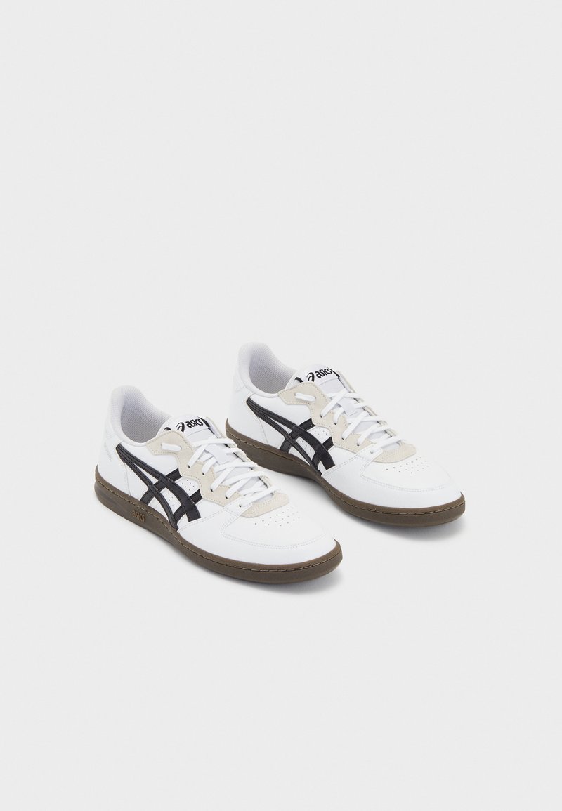 Adidași albi din material sportiv, cu accente negre, zonă de sârmă bej și talpă de cauciuc maro. Prezintă detalii perforate și elemente de design clasice.
