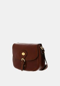 Borsa a tracolla in pelle marrone con chiusura a pattina, finiture in oro e un badge rotondo con logo. Presenta una tracolla e una texture liscia.