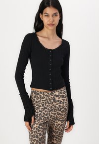 Svart ribbet langermet topp med knapper og scallop-halslinje; kombinert med leopardmønstrede bukser med elastisk stoff og en tettsittende silhuett.