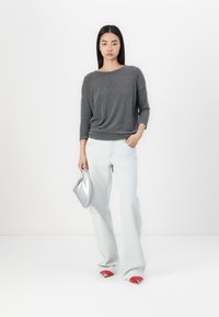 Grå, löst sittande långärmad topp, ljusblå utsvängda jeans, röda skor med detaljer, silverfärgad clutchväska, slät tyg, minimalistisk stil.