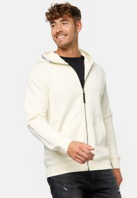 Crème zip-up hoodie met een contrasterende witte en zwarte capuchonrand. Beschikt over kangaroo zakken en ribgebreide manchetten, gemaakt van een zachte katoenmix.