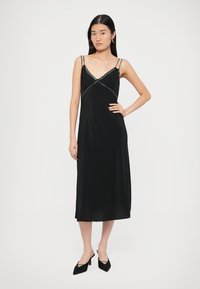 Melna satīna midi kleita ar V veida izgriezumu, plānām lencītēm un dekoratīvām sudraba pērlīšu uzlīmēm pie krūtīm. Gluda tekstūra un plūstošs dizains.