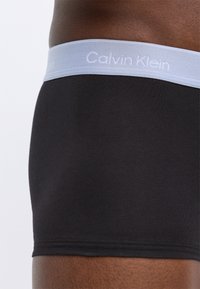 Fekete boxeralsó könnyű szürke rugalmas derékkal, rajta fehér "Calvin Klein" logóval. Simább, elasztikus anyagból készült.