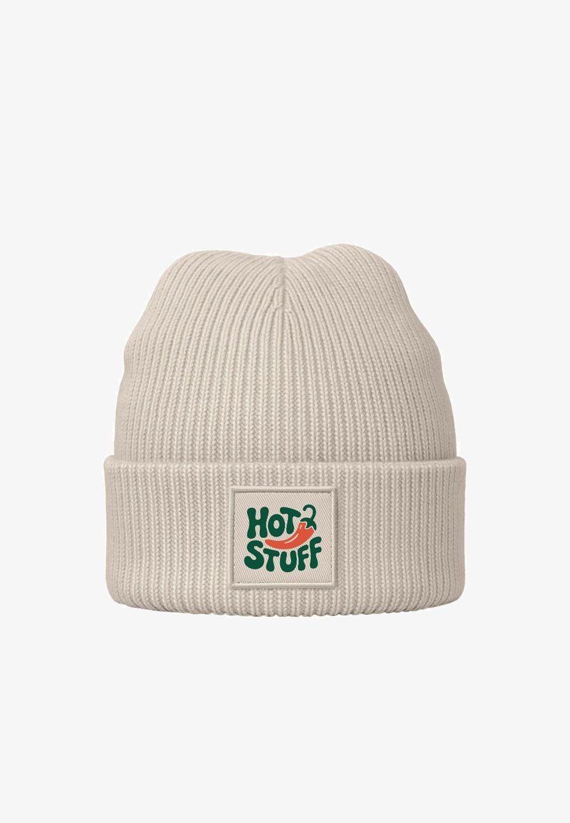 Knit beanie in light beige with a folded cuff. Features a green and red "HOT STUFF" logo on a cream label. Soft texture, ribbed design.