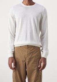 Maglione bianco leggero a maniche lunghe con tessuto testurizzato, scollatura rotonda e polsini a coste, abbinato a pantaloni cargo beige con tasche laterali.
