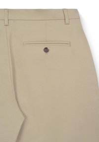 Beige maßgeschneiderte Hose mit einer einzigen Gesäßpaspeltasche mit einem dunkelbraunen Knopf und Gürtelschlaufen entlang des Bundes.