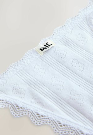 Vêtement en coton blanc avec texture côtelée et dentelle scallopée. Présente l'étiquette « self. » cousue en haut.
