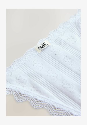 Vêtement en coton blanc avec texture côtelée et dentelle scallopée. Présente l'étiquette « self. » cousue en haut.