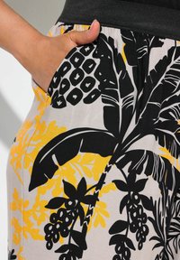 Černá a žlutá tkanina s květinovým vzorem a hladkým povrchem. Obsahuje elastický pas a detaily boční kapsy.