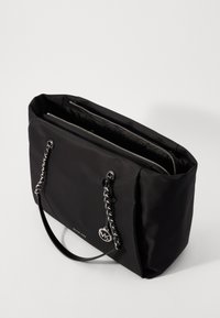 Sac fourre-tout noir en nylon avec des accents en chaîne argentée, fermeture zippée sur le dessus, doubles poignées et un pendentif logo. Texture lisse, forme rectangulaire.