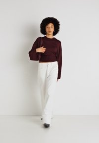 Sweater curto em bordeaux, calças brancas de perna larga e sapatos pretos. O sweater apresenta mangas compridas e um acabamento texturizado.