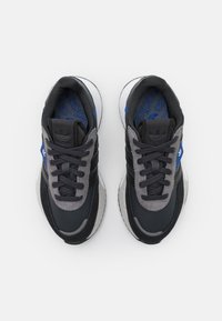 Svarta och grå sportskor med en texturerad överdel, blå accenter och en vit sula. Har snören och logodetaljer på tungan.