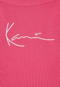 Rosa ribbestrikket stoff med hvit brodert signatur. Teksturen er glatt med vertikale linjer som fremhever designets visuelle tiltrekningskraft.