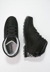 Botas de senderismo negras con una parte superior de cuero suave, forro blanco en contraste, cordones redondos y suela de goma resistente con un agarre texturizado.
