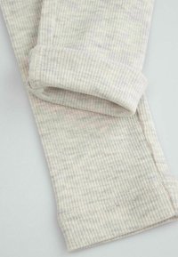 Ściśle żebrowany jasnoszary materiał z delikatnym nakrapianym wzorem, z wywiniętym mankietem i starannym detalem przeszycia.