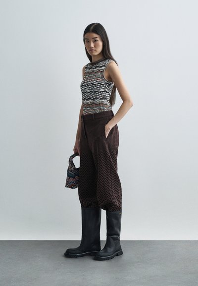 Ärmlös mönstrad topp med vågiga ränder i svart, brunt och grått; bruna hundtandsmönstrade vida byxor; svarta knähöga stövlar; liten mönstrad väska.