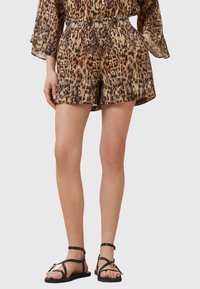Leopard print short set in shades of brown and beige, featuring an elastic waistband and flowy sleeves, paired with black strappy sandals.