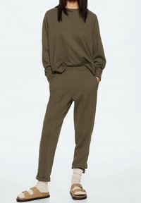 Sweatshirt vert olive à coupe ample, col côtelé ; pantalons de survêtement assortis à coupe fuselée avec poches latérales ; sandales beiges et chaussettes épaisses en tricot.