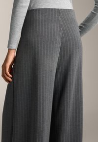Szare spodnie w szerokim kroju wykonane z miękkiego materiału mają pionowy wzór w prążki. Pas posiada gładką teksturę, a kieszenie są wkomponowane w design.