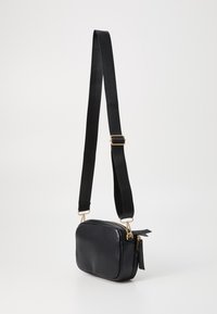 Geantă crossbody din piele neagră, cu o formă rectangulară, accesorii aurii și o curea ajustabilă neagră. Dispune de închidere cu fermoar și detalii cu ciucuri pe lateral.