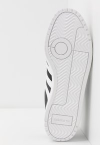 Svart och vit sneaker med en texturerad gummisula, prydd med tre svarta ränder och en Adidas-logotyp på sidan.