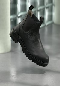 Black leather ankle boot with a textured upper, elastic side panels, and a chunky rubber outsole. Features pull tabs for easy wear.