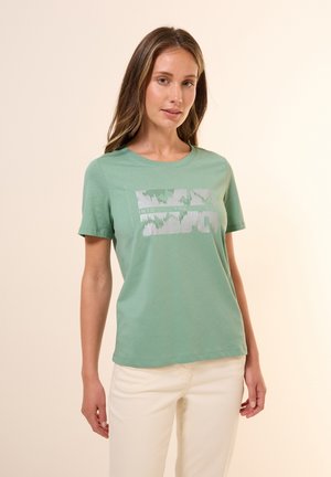 T-shirt en coton vert clair avec des manches courtes et un col rond. Présente un imprimé graphique en texte argenté, conçu pour un port décontracté.