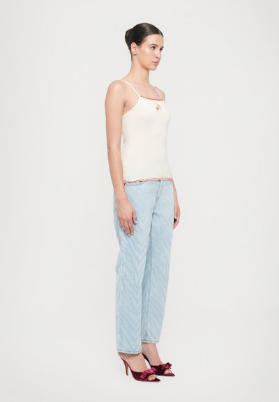 Beige toppi spaghetti-straps med en orange bølget kant, parret med lyseblå jeans med zigzag-mønster og burgunder højhælede sko med sløjfer.