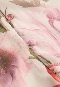 Détail d'un tissu floral présentant des teintes douces de rose et de vert, avec des boutons ronds roses et un motif tissé légèrement texturé.