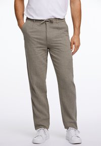 Pantalons gris clair, texturés, avec une taille élastique et un cordon de serrage. Poches latérales et coupe décontractée. Associés à des baskets blanches.