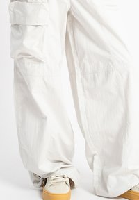 Białe spodnie cargo o luźnym kroju, z bocznymi kieszeniami i elastycznymi mankietami. Zestawione z jasnymi sneakersami na gumowej podeszwie.