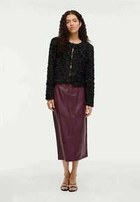 Svart texturerad kofta med blommönster, knappstängning, i kombination med en lång bourgogne läderkjol och svarta sandaler med remmar.