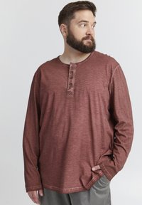Camisetta henley a maniche lunghe color marsala, realizzata in cotone testurizzato, con scollatura rotonda e patta con tre bottoni. Slim-fit con orlo arrotondato.